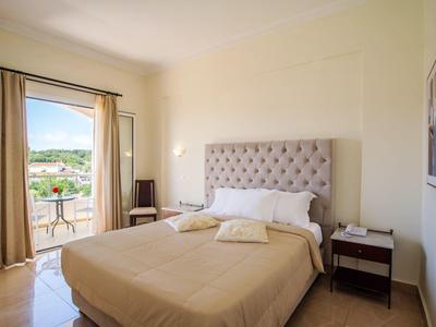 Hell eingerichtetes Hotelzimmer mit Doppelbett, Balkon und Blick auf grüne Hügel.