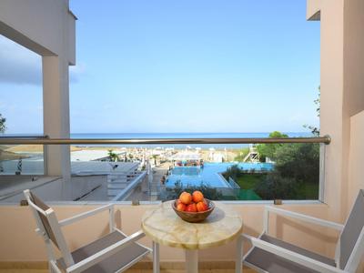 Balkon mit zwei Stühlen, Tisch und Blick auf Pool und Meer in einem Hotelzimmer.