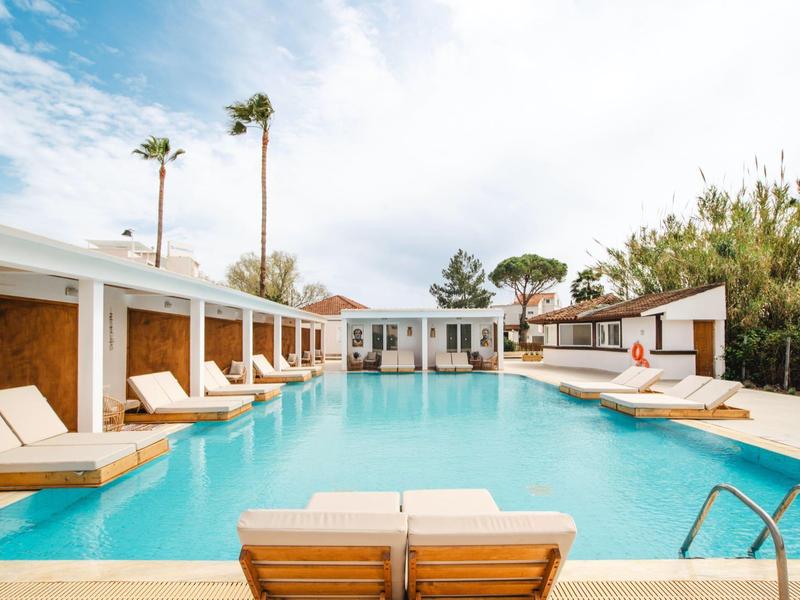 Moderní venkovní bazén s lehátky a palmami před bílou budovou.