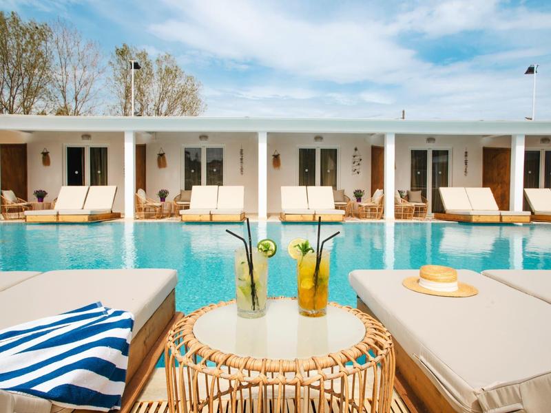 Moderní bazénová část s lehátky a nápoji před hotelem s řadou pokojů.