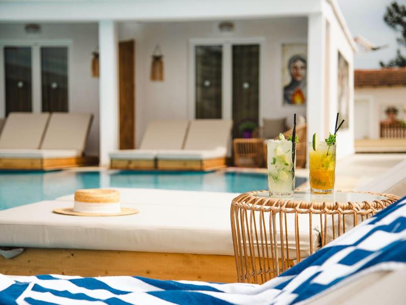 Relaxační prostor u bazénu s lehátky, nápoji a dekoračním interiérem v pozadí.