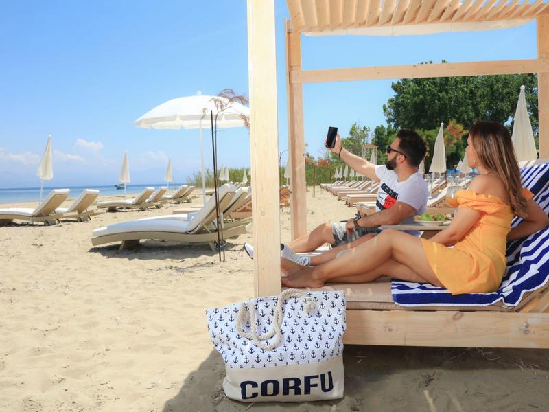 Dvě ženy relaxují na pláži pod pergolou s výhledem na moře.