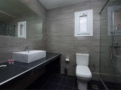 Modernes Badezimmer mit grauen Fliesen, großer Spiegel, weißem Waschbecken, WC und Glasdusche.