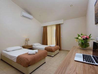 Einfaches Hotelzimmer mit zwei Einzelbetten, Tischlampen, Laptop und Blumenvase auf Schreibtisch.