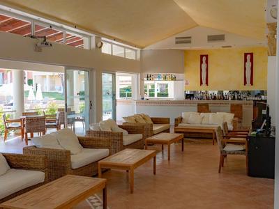 Großer Hotel-Loungebereich mit Holzmöbeln, großen Fenstern und gelben Wänden.