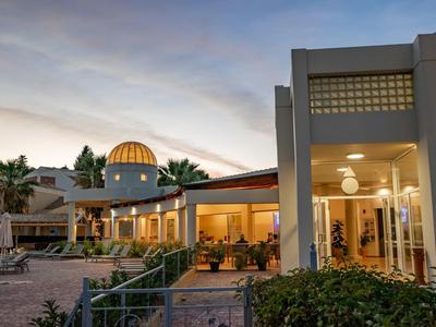 Außenbereich eines Hotels bei Sonnenuntergang mit Sitzbereich und beleuchtetem Gebäude.