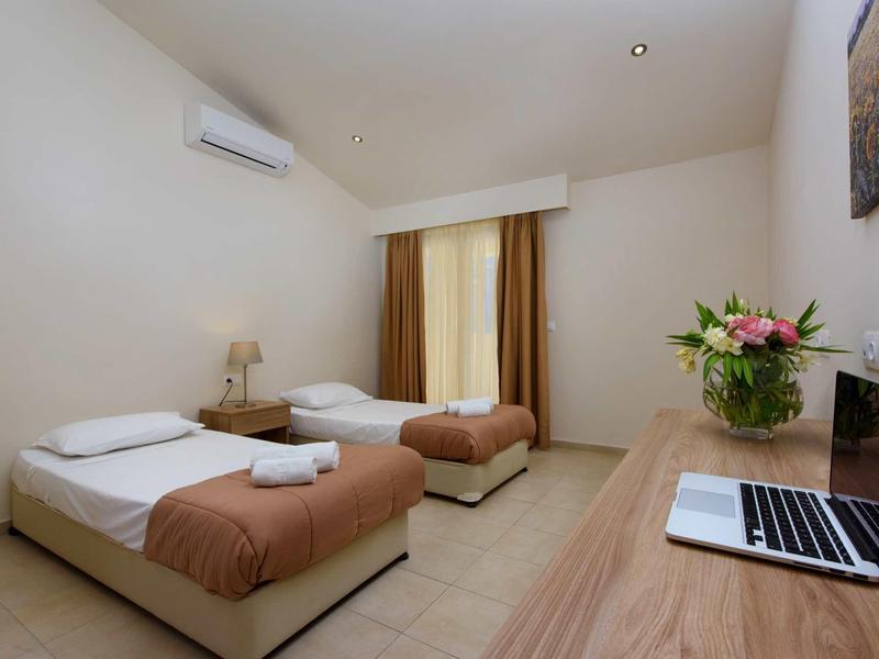 Einfaches Hotelzimmer mit zwei Einzelbetten, Tischlampen, Laptop und Blumenvase auf Schreibtisch.