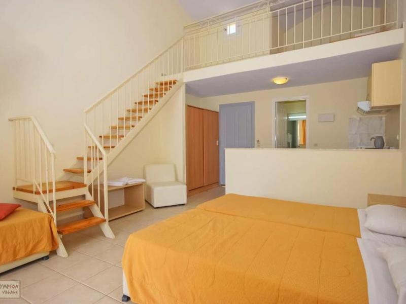 Zimmer mit zwei Betten, Treppe zur Galerie, Küche, beige Möbel und orangefarbene Bettdecken.