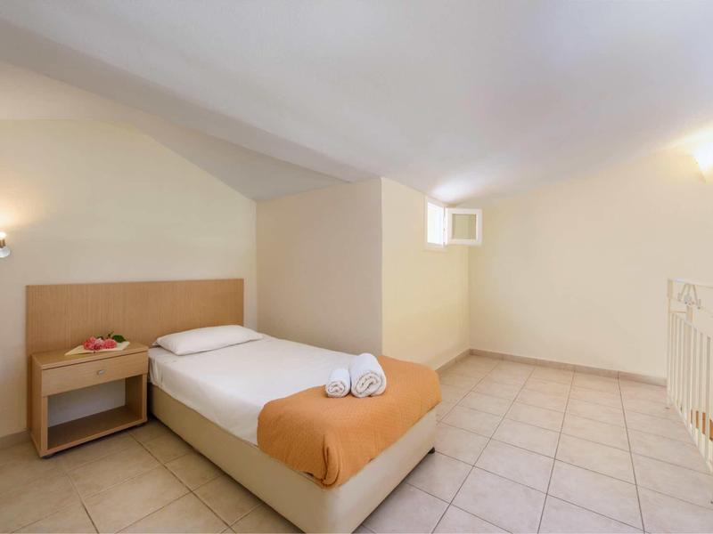 Kleines Zimmer mit Einzelbett, orangener Decke, Nachttisch und schräger Decke, helle Fliesenboden.