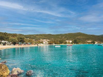 Agua turquesa clara frente a una playa de arena con colinas al fondo y cielo azul.