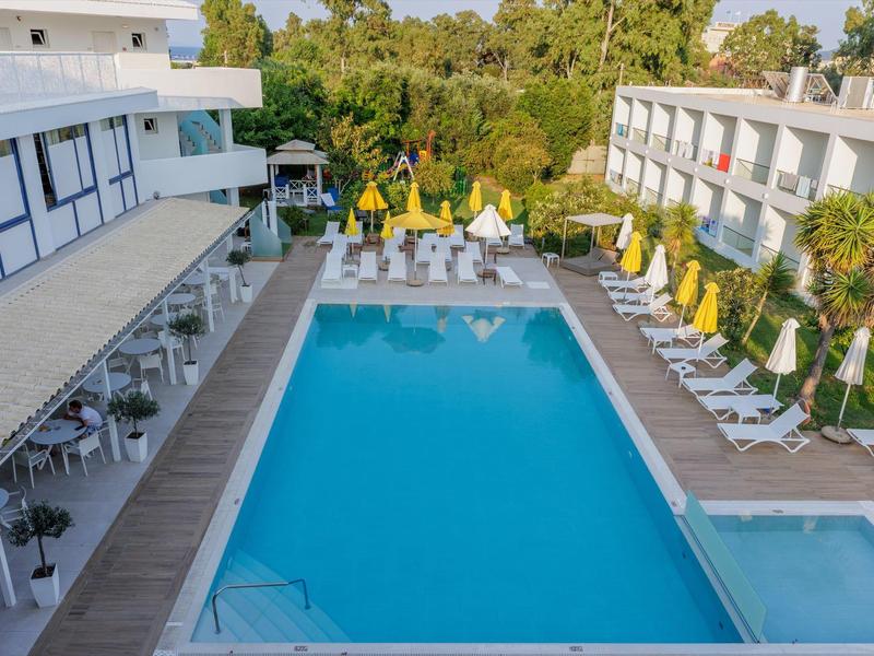 Outdoor hotel pool area with lounge chairs and yellow umbrellas surrounded by greenery.