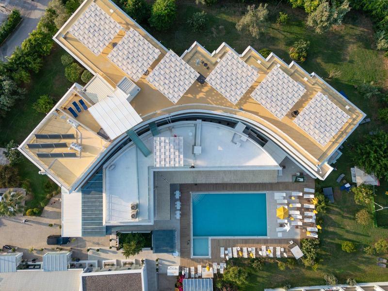 Aerial view of a hotel with a rooftop terrace and a rectangular swimming pool surrounded by sunbeds.