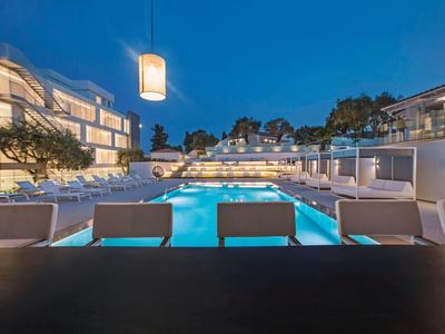 Modern buitenzwembad met ligstoelen en verlichting in stijlvolle hotelsfeer bij schemering.