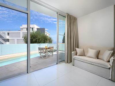 Moderne kamer met bank, raampartij tot aan de grond en terras met zwembad en zithoek.