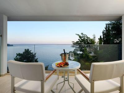 Balkon met twee stoelen en tafel met drankjes, uitzicht op zee bij zonsondergang.