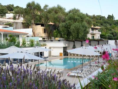 Moderner Poolbereich mit Sonnenliegen und weißen Sonnenschirmen vor einem Hotelgebäude mit Bäumen.