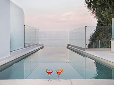 Moderner Pool mit Glasgeländer und zwei Cocktails bei Sonnenuntergang.