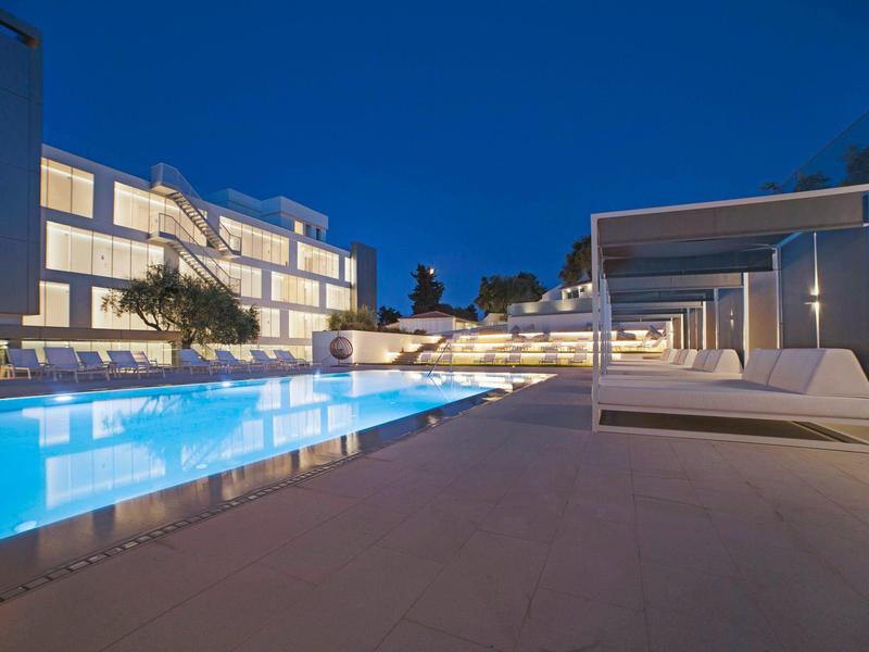 Modern hotelzwembad 's nachts met verlicht water en comfortabele ligbedden.