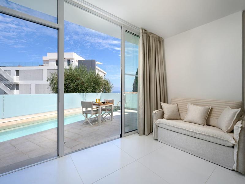 Moderne kamer met bank, raampartij tot aan de grond en terras met zwembad en zithoek.