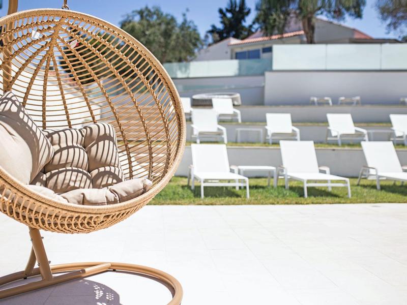 Ronde rotan stoel met kussens buiten voor witte ligstoelen op een zonnige dag.