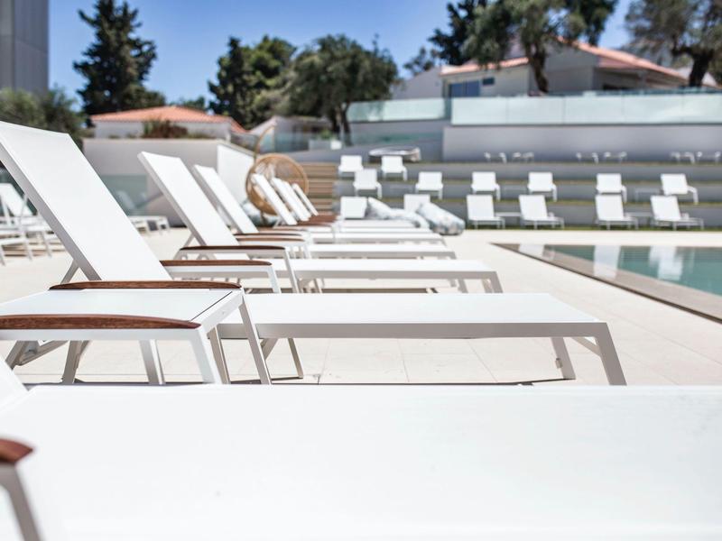 Rij witte ligstoelen naast een zonnig zwembad bij een hotelresort.