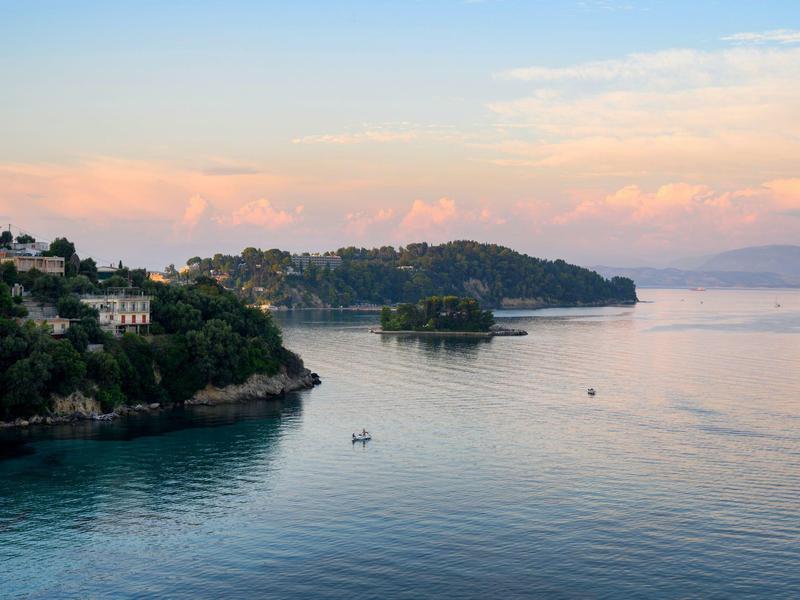 Uitzicht op een rustige baai met eilanden en een zachte zonsondergang op de achtergrond.