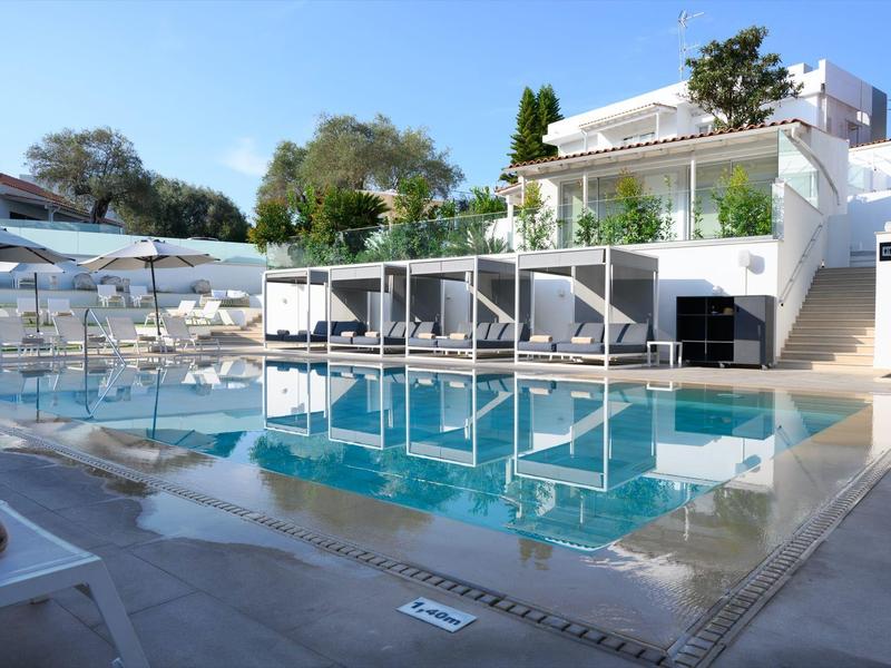 Modern hotelzwembad met ligbedden en cabana's onder een blauwe lucht.