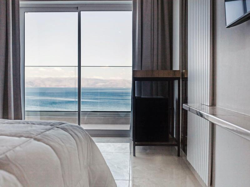 Hotelkamer met groot raam met uitzicht op zee en de lucht aan de horizon.