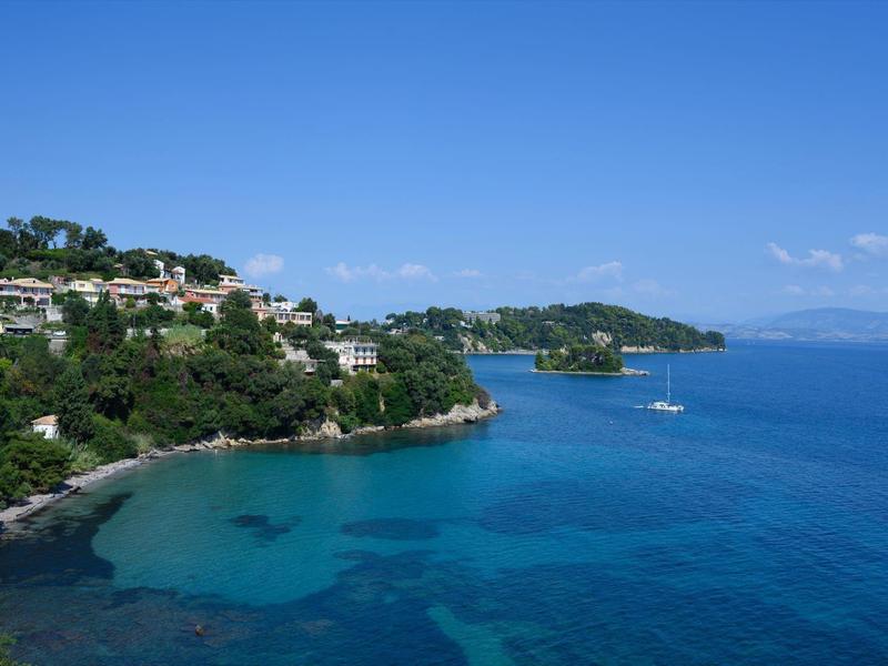 Kustlijn met helder blauw water, groene heuvels met huizen onder een blauwe lucht