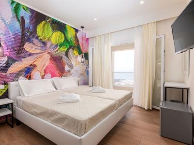 Modernes Schlafzimmer mit großem Bett, bunter Wandgestaltung und einem Fenster mit hellem Vorhang.