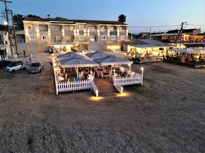 Buitengebied van een restaurant met verlichte zitplaatsen en een wit gebouw op de achtergrond bij zonsondergang.