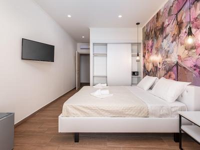 Moderní hotelový pokoj s manželskou postelí, květinovou nástěnnou malbou a televizí na zeď.