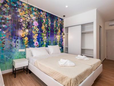 Moderní ložnice s manželskou postelí, květinovou tapetou a otevřenou skříní v hotelovém pokoji.