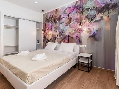 Moderní hotelový pokoj s manželskou postelí, květinovým vzorem na zdi a otevřenou skříní.