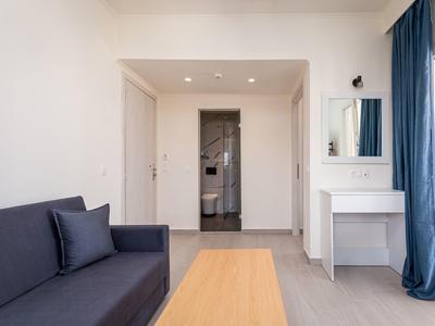 Světý hotelový pokoj s tmavým gaučem, dřevěným stolem a bílým toaletním stolkem se zrcadlem.