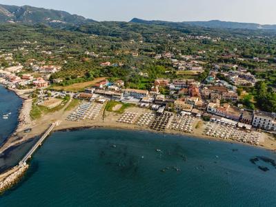 Letecký pohled na pobřežní vesnici s plážovými lehátky a okolními kopci.