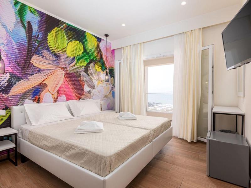 Moderní hotelový pokoj s velkou postelí, barevným nástěnným malbou a výhledem na moře.