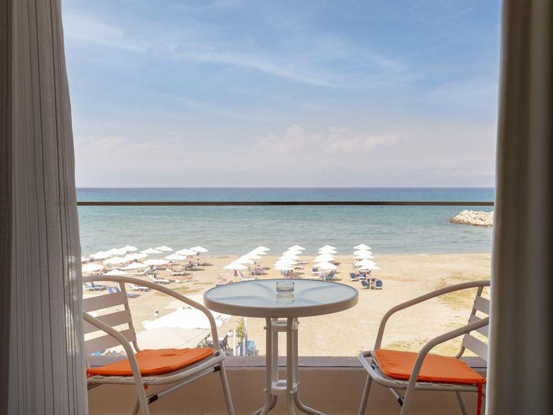 Výhled na moře s písečnou pláží a židlemi z okna hotelového pokoje.