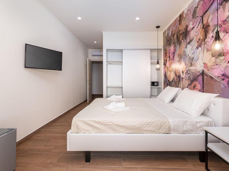 Moderní hotelový pokoj s manželskou postelí, květinovou nástěnnou malbou a televizí na zeď.