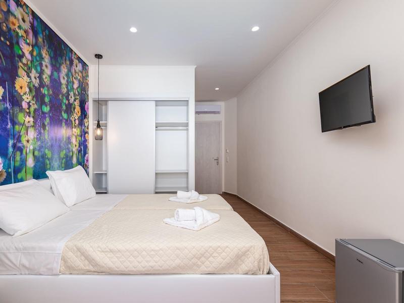 Moderní hotelový pokoj s manželskou postelí, barevným nástěnným uměním a televizí s plochou obrazovkou.