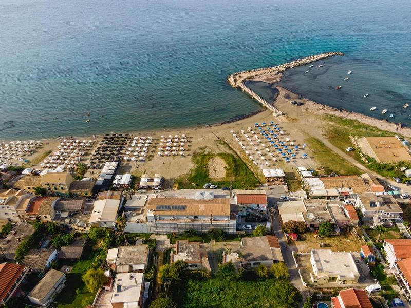 Letecký pohled na pláž s lehátky, budovami a přístavem.