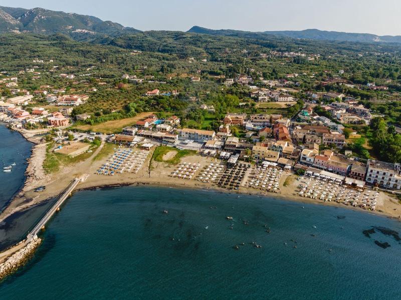 Letecký pohled na pobřežní vesnici s plážovými lehátky a okolními kopci.