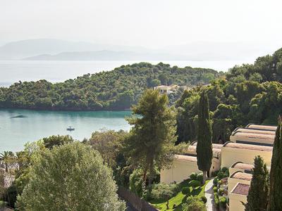 Vue sur une baie calme avec des pins et des bâtiments d'hôtel dans un paysage méditerranéen.
