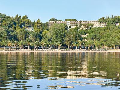 Complex hôtelier avec plusieurs bâtiments sur une colline boisée au bord d'un plan d'eau calme.