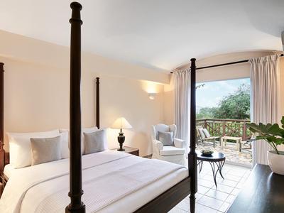 Chambre d'hôtel élégante avec lit à baldaquin, fauteuils et balcon avec vue sur la nature.