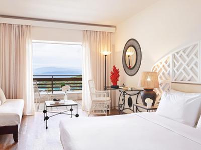 Chambre d'hôtel lumineuse avec lit double, balcon et vue sur la mer, décoration moderne.