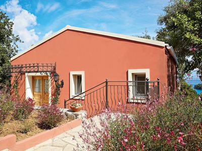 Maison de vacances rouge avec balcon et jardin sous un ciel bleu.