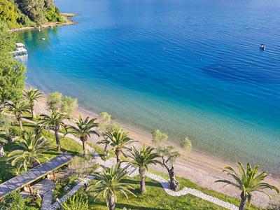 Palmbomen omringen een tropisch zandstrand met helderblauw water en groene kustlijn.