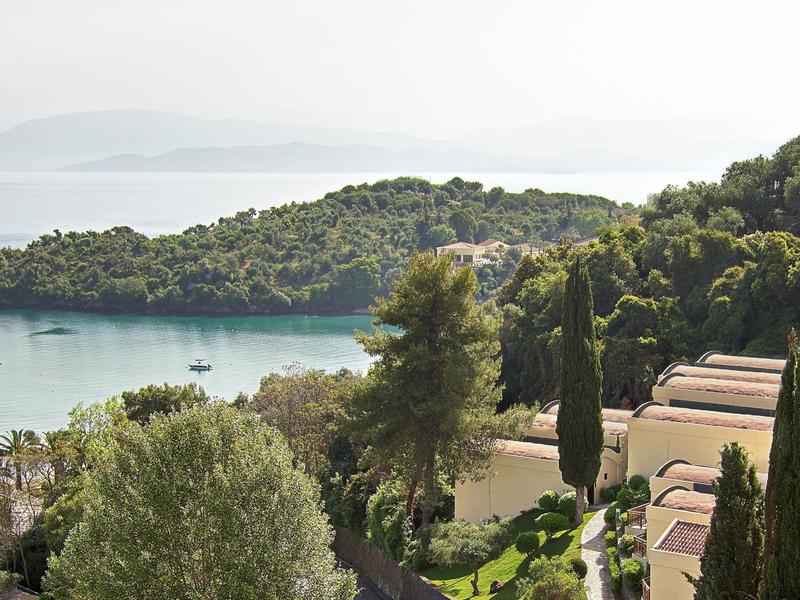 Vue sur une baie calme avec des pins et des bâtiments d'hôtel dans un paysage méditerranéen.