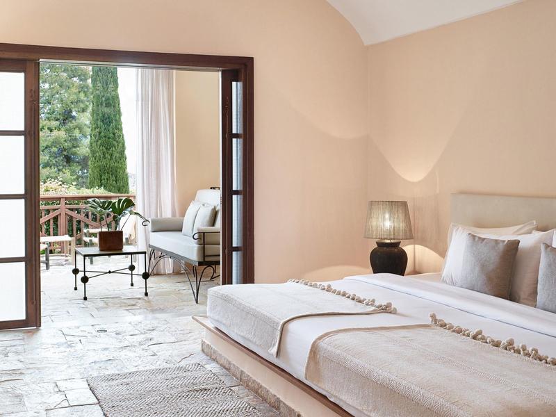 Chambre d'hôtel lumineuse avec un lit confortable et vue sur une terrasse avec un coin salon et un jardin verdoyant.